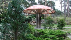 Ein Laternenpfahl mit einem roten Regenschirm in einem Garten.
