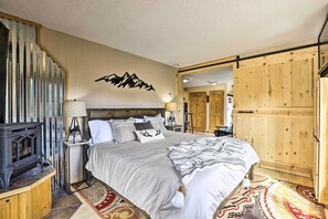 A cozy bedroom with a bed, a wooden wardrobe, a fireplace, and a patterned rug.