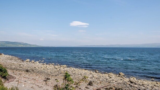 Eine felsige Küstenlinie mit ruhigem Meer und sanften Hügeln im Hintergrund.