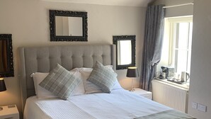 Ein ordentlich eingerichtetes Schlafzimmer mit einem großen Bett, zwei Nachttischen, einem Fenster mit Vorhängen und einem Heizkörper.