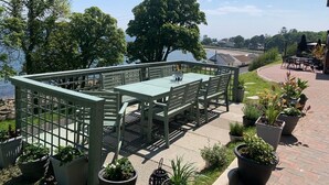 Eine Terrassengruppe im Freien mit Tisch und Stühlen, umgeben von Pflanzkübeln und mit Blick auf ein Gewässer.