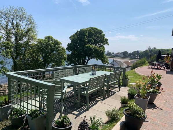 An outdoor patio with a table and chairs, surrounded by potted plants and overlooking a body of water.