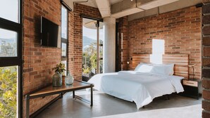 Een moderne slaapkamer met zichtbare bakstenen muren, een groot bed, een aan de muur bevestigde televisie en uitzicht op de omgeving.