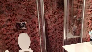 Une salle de bain avec un mur recouvert de mosaïques, des toilettes, un espace douche et un lavabo avec un miroir.