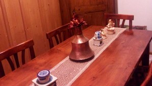 Une table à manger en bois, agrémentée d’un chemin de table en dentelle, d’un vase avec des fleurs et d’une petite figurine.