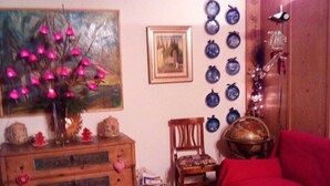 Une pièce comprenant une commode en bois, un canapé rouge, un tapis à motifs, un tableau et un mur décoré d’assiettes bleues.