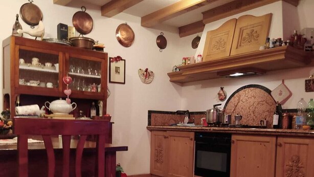 Une cuisine traditionnelle avec des meubles en bois, une table à manger avec des chaises et un tapis rouge à motifs.