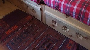 Un lit simple avec une couvre-lit à carreaux rouges et blancs, une tête de lit en bois, une horloge murale, un tableau encadré et un tapis à motifs sur le sol.