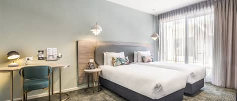 Una habitación de hotel con dos camas, un escritorio con silla, una mesita pequeña y un teléfono instalado en la pared.
