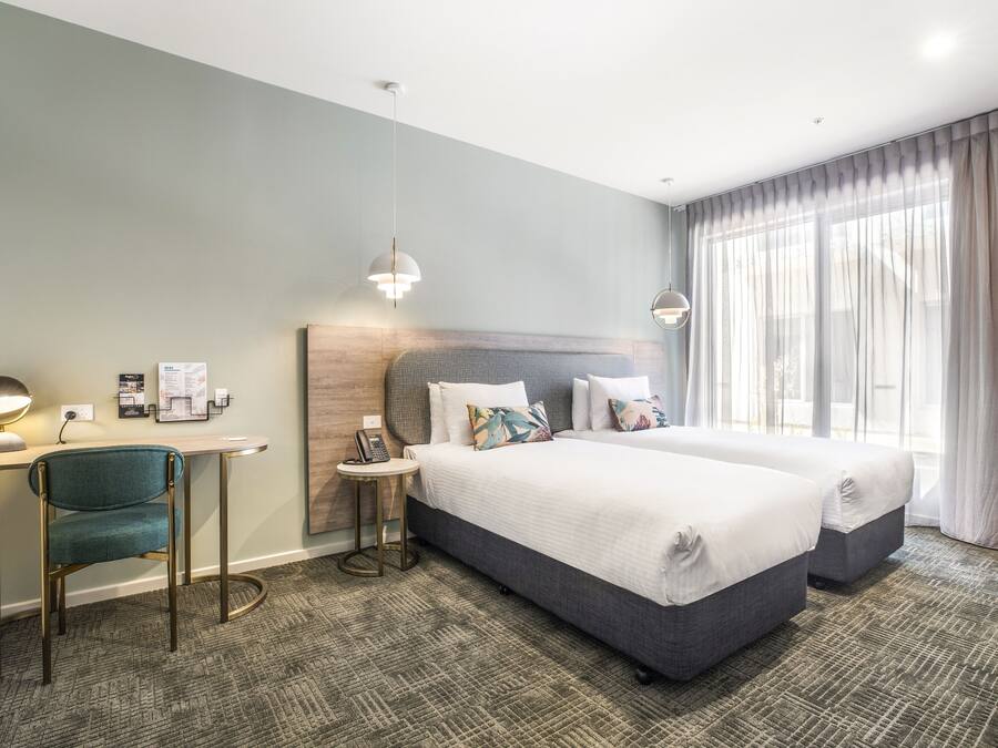 A hotel room with two beds, a desk with a chair, a small table, and a wall-mounted phone.
