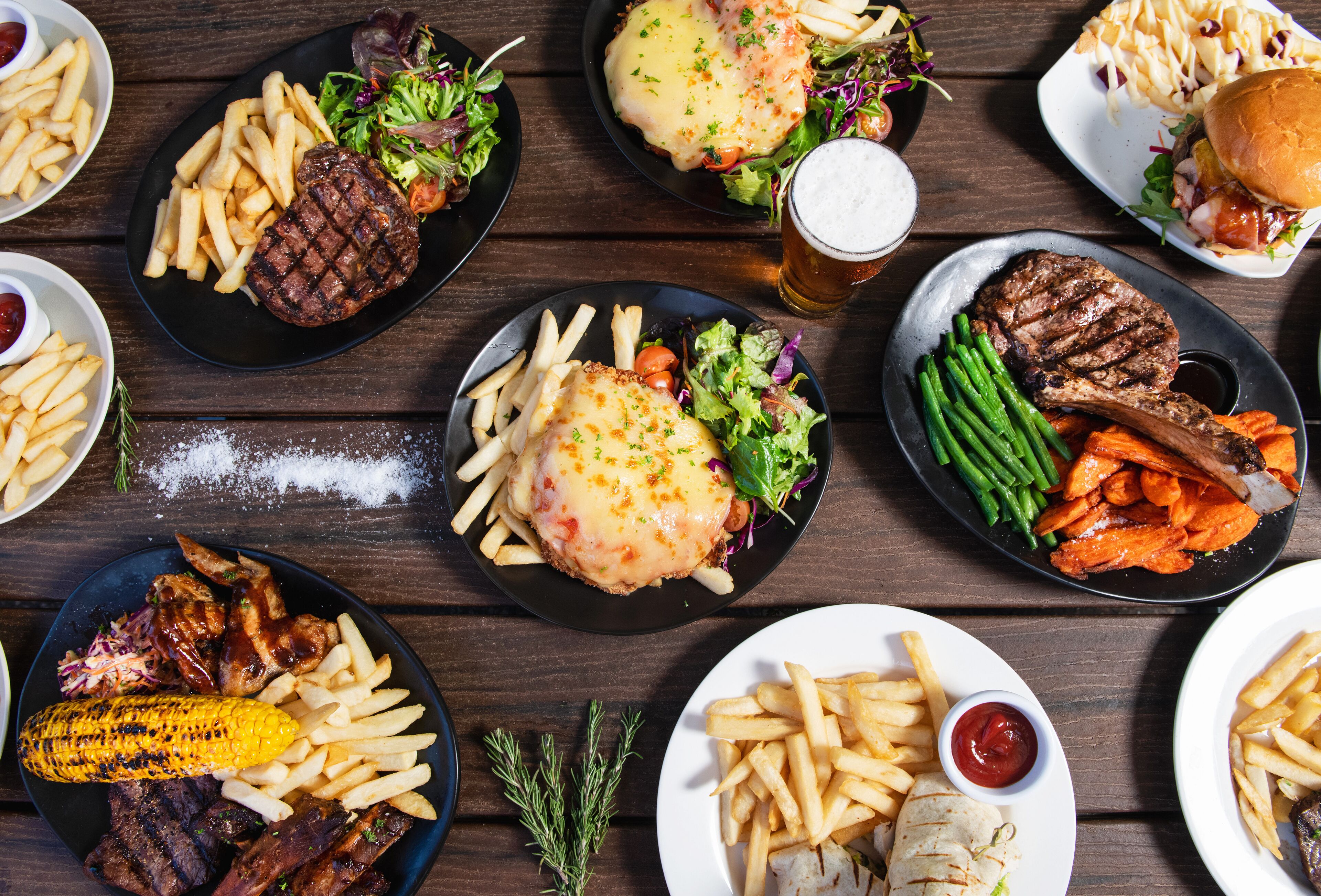 Une variété de plats, notamment des hamburgers, des frites et des viandes grillées, disposés sur une table en bois.