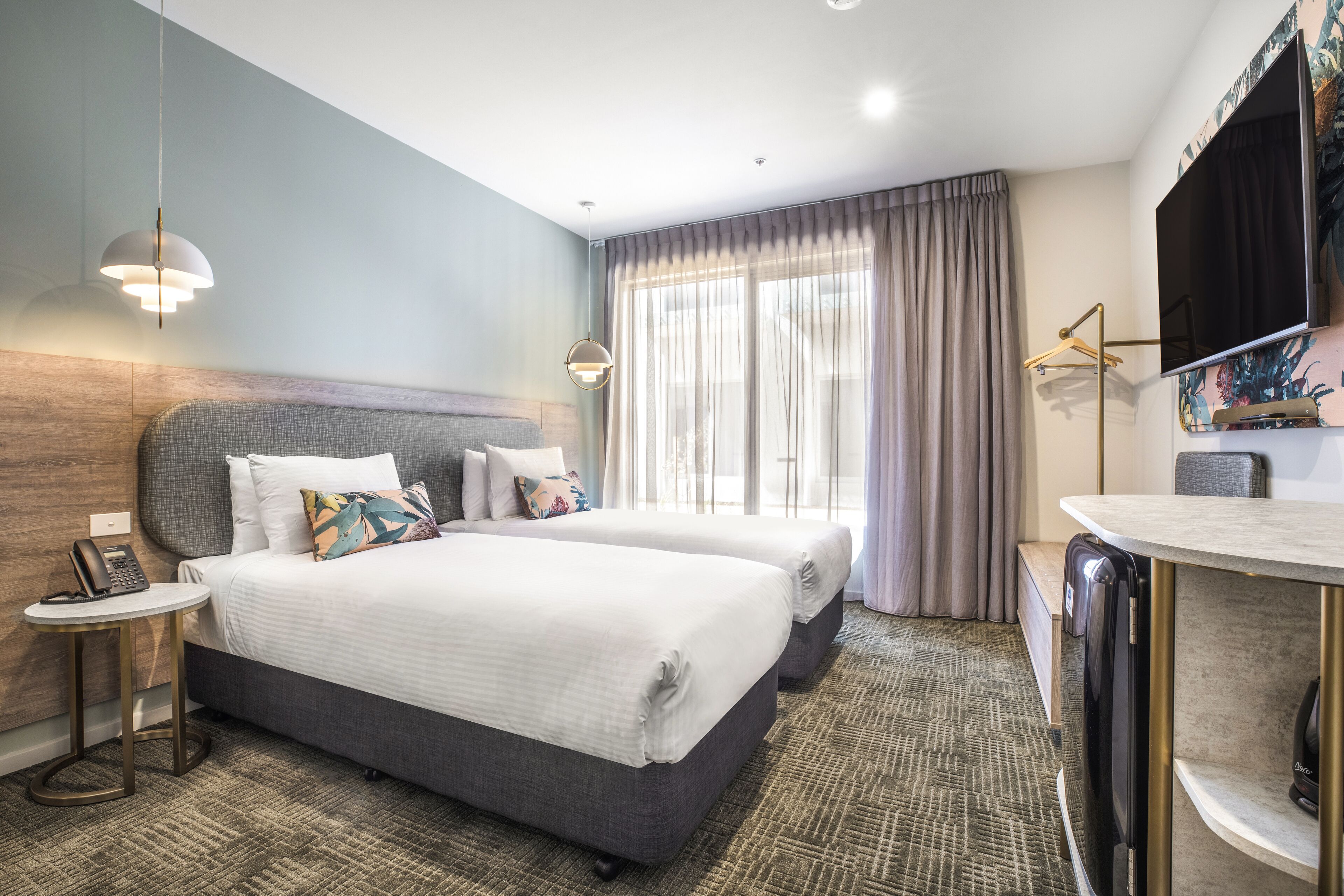 A hotel room with two beds, a desk, a flat-screen TV, and a telephone on a side table.