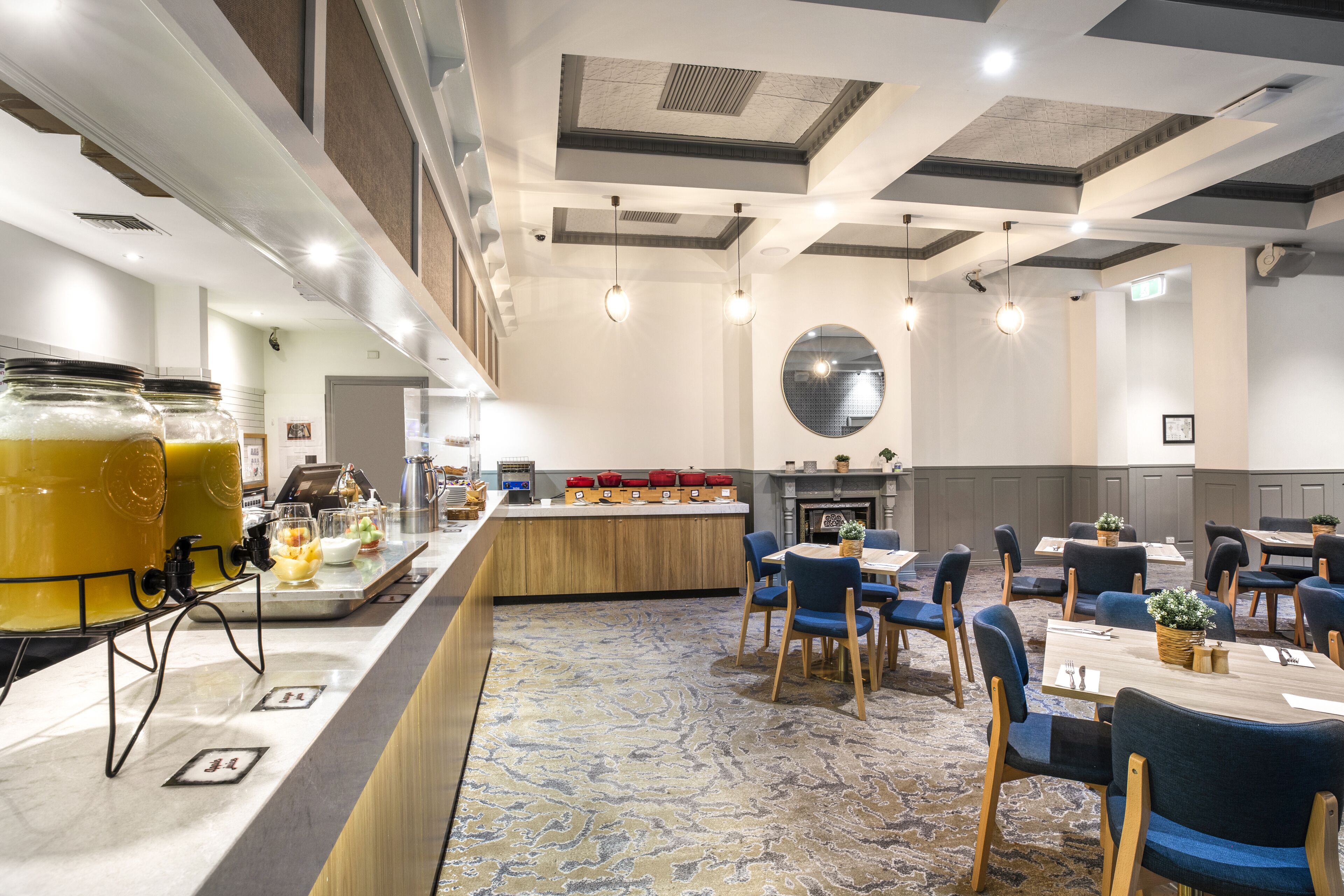 Een restaurantgedeelte in een hotel met een buffet, ronde tafels en stoelen.