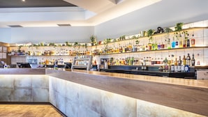 Zona de bar moderna con una barra larga, estanterías llenas de botellas de licor y plantas decorativas.