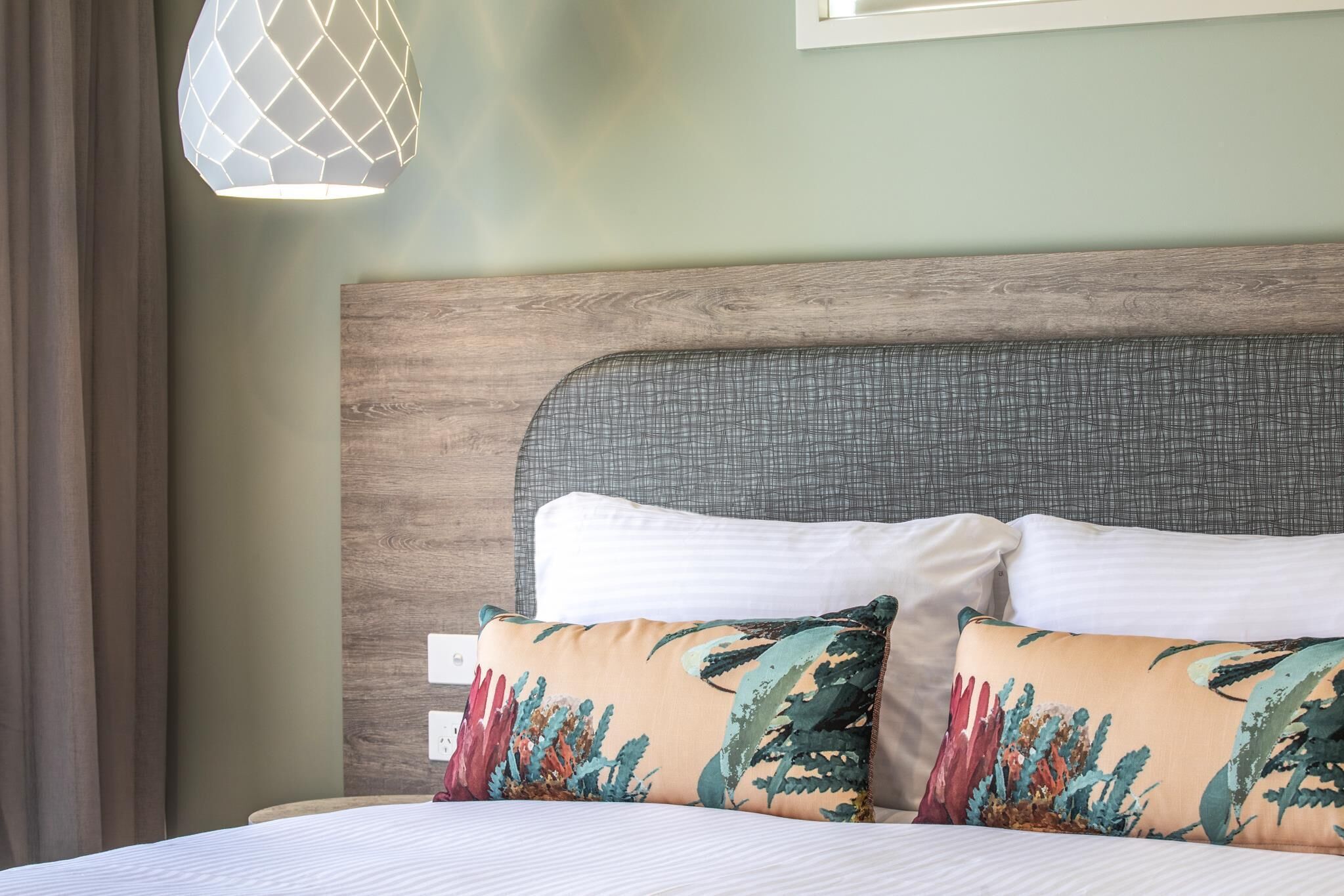Una cama bien hecha con dos almohadas, cabecera de madera y una lámpara colgante.