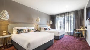 Habitación de hotel con dos camas, una mesita, una silla y un televisor.