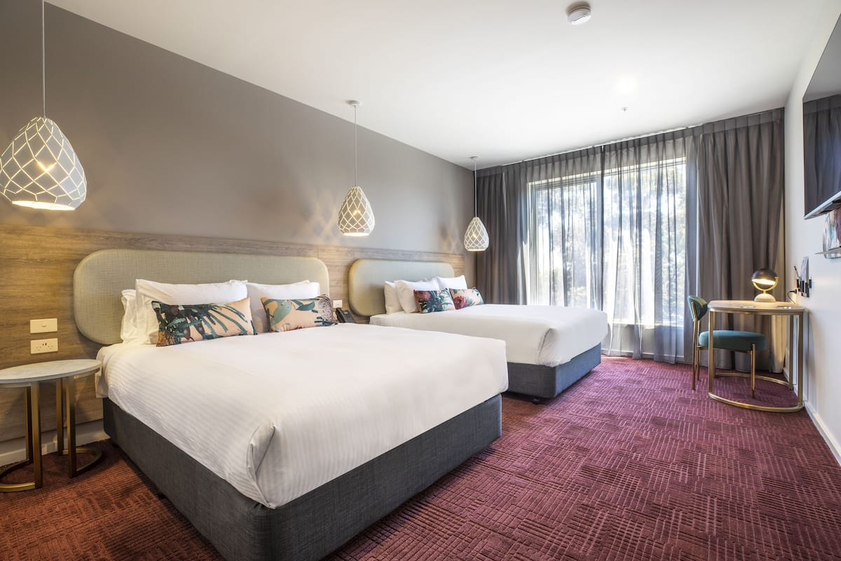 Ein Hotelzimmer mit zwei Betten, einem kleinen Tisch, einem Sessel und einem Fernseher.