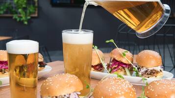 A table with a tall glass of beer, a pitcher pouring beer, and several burgers.