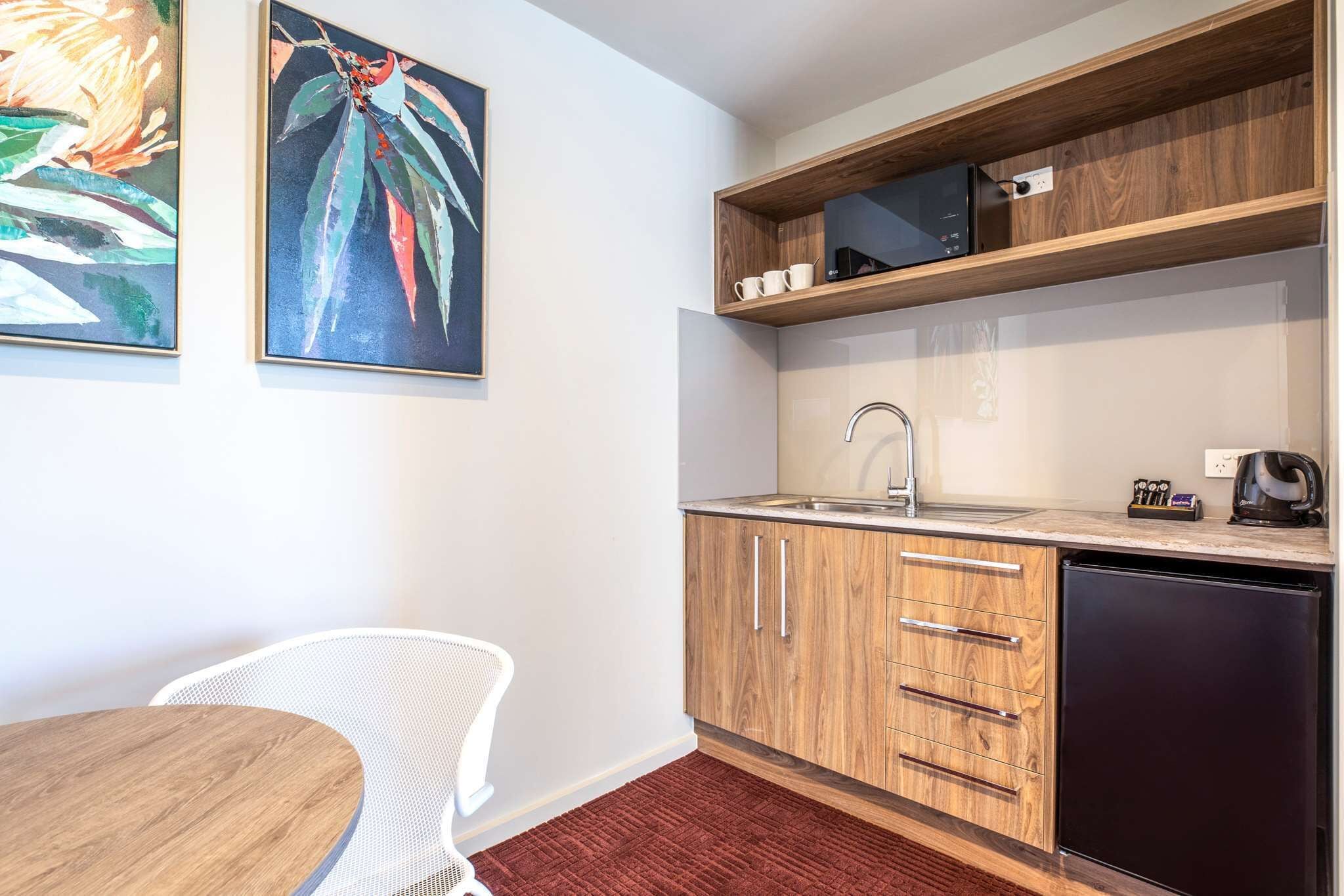 Une cuisine de taille réduite, avec des meubles de rangement en bois, un évier et un four à micro-ondes posé sur une étagère.