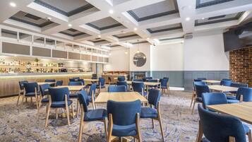 Un comedor amplio con varias mesas y sillas, una barra con diversas bebidas y un diseño moderno de techo.