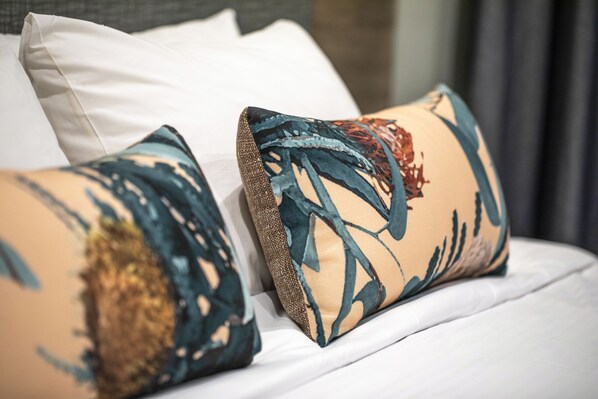 Una cama con sábanas blancas y dos almohadones decorativos con diseños abstractos.