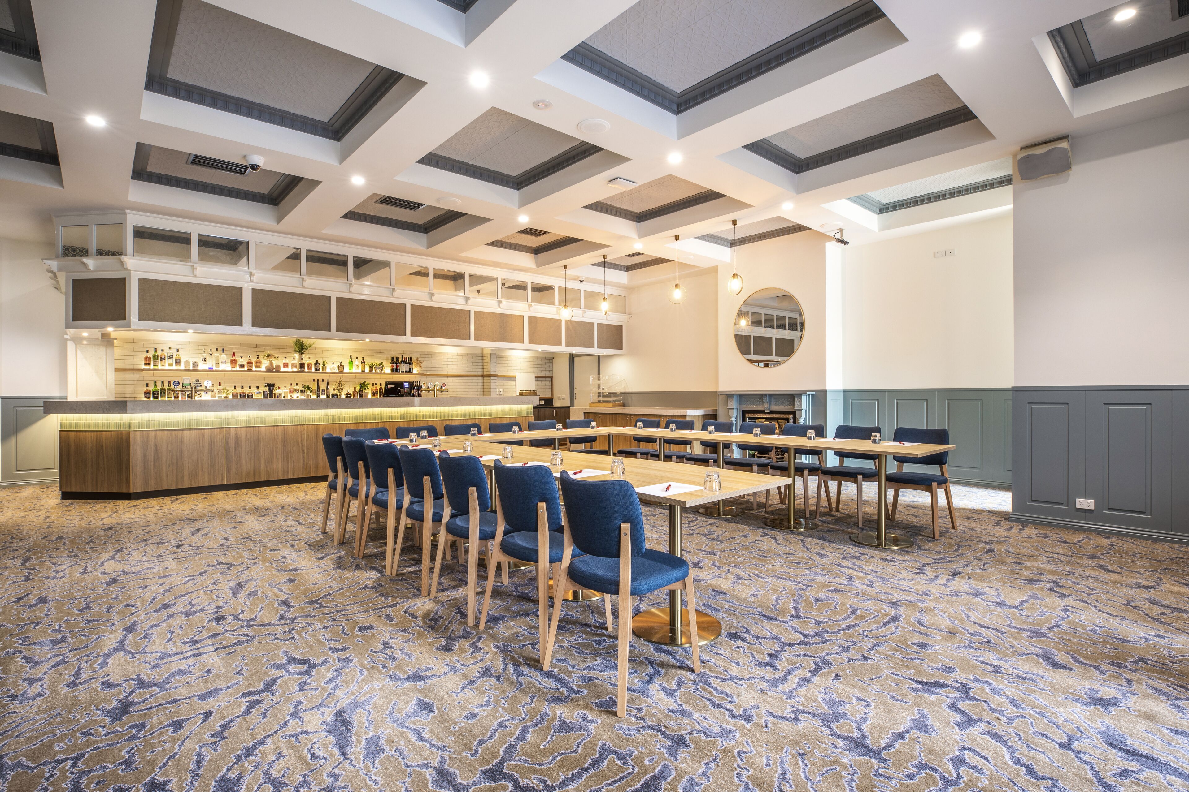 A conference room with a long table, blue chairs, and a bar area with shelves of bottles.