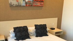 A neatly made bed with white linens and two black pillows, a bedside table with a lamp, and a wall art piece above the bed.