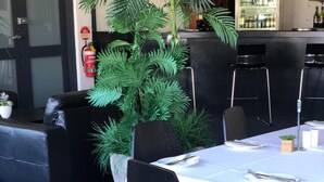 A restaurant setting with a table set for two, black chairs, a white tablecloth, and a potted plant.