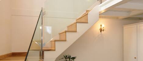A staircase with glass railings, a wooden desk with a chair, a vase with a plant, and a patterned floor.