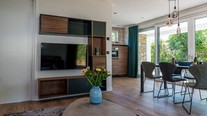 Un salon moderne doté d’un téléviseur à écran plat, d’un vase bleu orné de fleurs et d’un coin repas avec des chaises et une table.