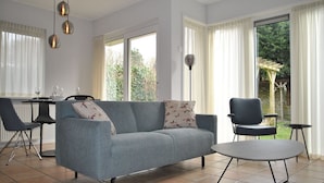 Un salon moderne avec un canapé gris, une table basse ronde et un coin repas comprenant une table et des chaises.