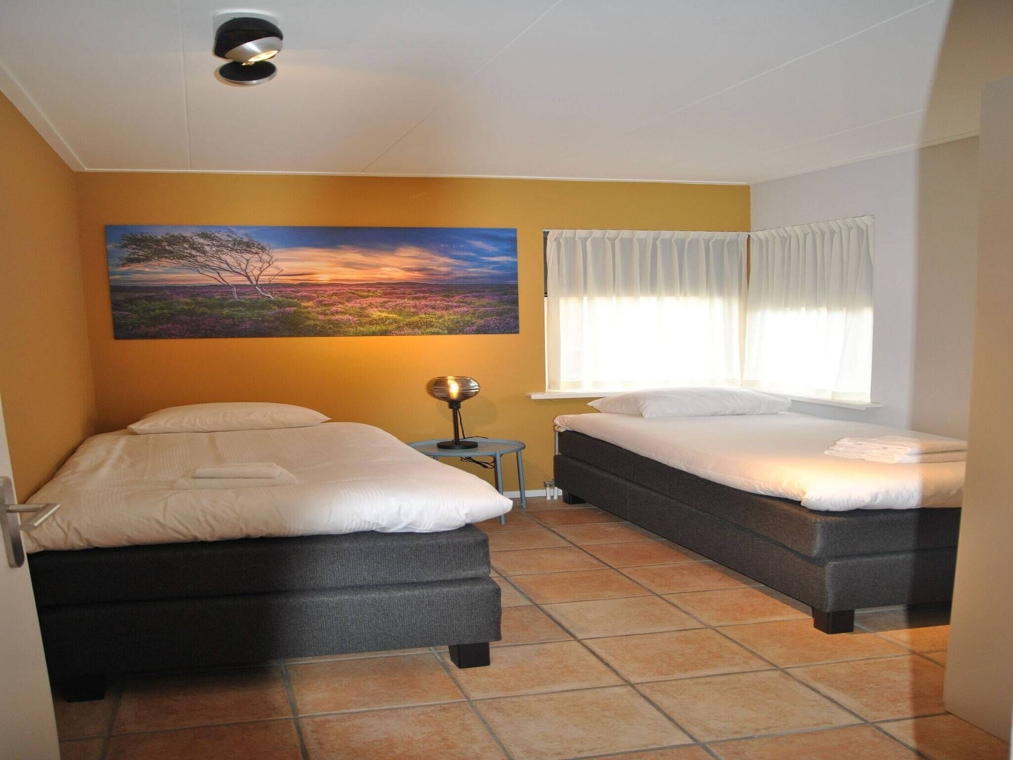 A hotel room with two beds, a painting on the wall, a lamp, and a window with curtains.