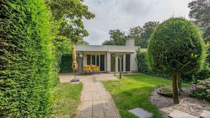 Une maison moderne dotée d’un patio, d’une petite table avec des chaises et d’une pelouse soigneusement entretenue.