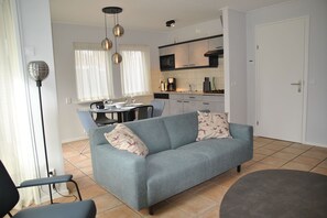 A modern living room with a sofa, a dining table, and a kitchen in the background.