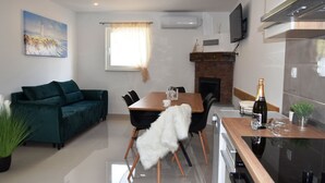 Ein modernes Wohnzimmer mit einem grünen Sofa, einem Esstisch mit Stühlen, einem Kamin und einer Küchenzeile inklusive Fernseher und Klimaanlage.