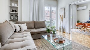 En moderne stue med en beige sofa, et glasbord og et spiseområde med orange stole.