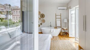 Et moderne badeværelse med et fristående badekar, et toiletbord og et stort vindue med udsigt over byen.