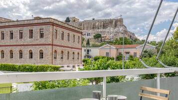 A balcony with a table and chairs overlooking a historic building and a rocky hill.