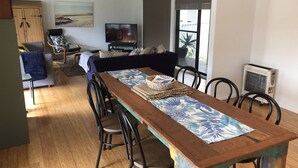 A dining area with a wooden table, chairs, and a TV in the background. - Sandy Shores - popular location (Vincentia)