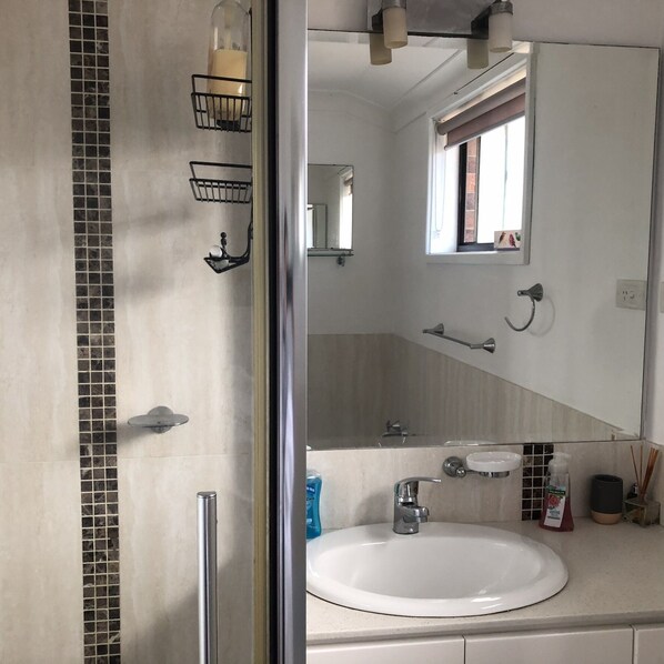 A bathroom with a large mirror, a sink, and a shower area. - Sandy Shores - popular location (Vincentia)