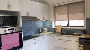A modern kitchen with white cabinets, a stainless steel microwave, a kettle, and a sink. - Sandy Shores - popular location (Vincentia)