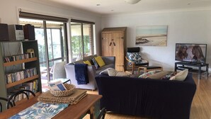 A living room with a sofa, a coffee table, a bookshelf, and a television. - Sandy Shores - popular location (Vincentia)