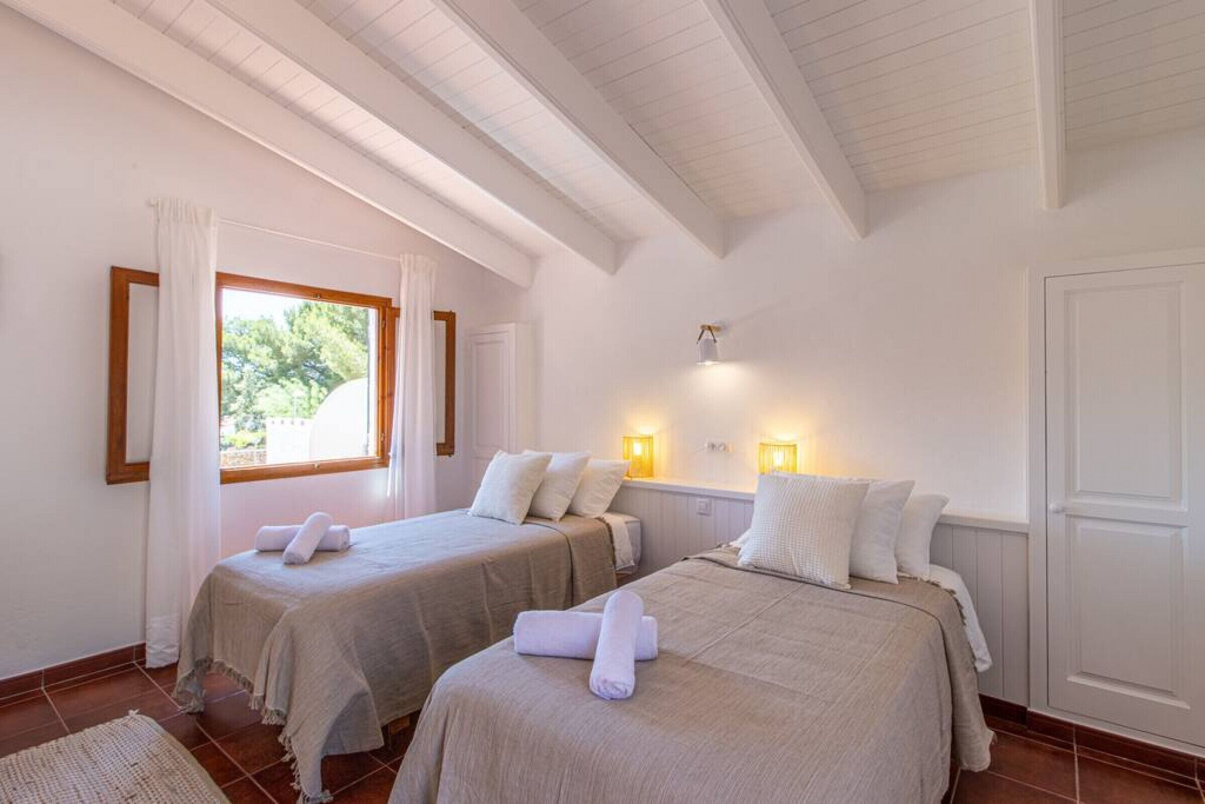 A room with two beds, a window with curtains, and wall-mounted lights.