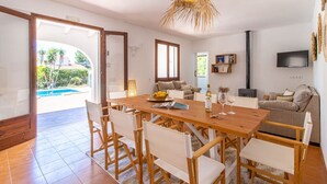 Uma sala de jantar ampla, com mesa e cadeiras de madeira, televisão na parede e vista para a piscina exterior.