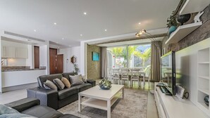 Una sala de estar moderna con un sofá de cuero negro, una mesita de centro blanca y un televisor sobre un mueble blanco.