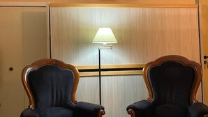 Et værelse med to polstrede stole med træstel, en gulvlampe og en dør.