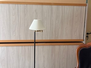 A room with a wooden wardrobe, a floor lamp, and a chair.