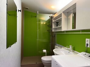A bathroom with a green shower enclosure, a white toilet, a white sink, and a mirror above the sink.