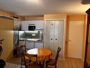 A compact kitchen with a sink, microwave, and cabinets. There is a dining table with chairs and a door leading to another room.
