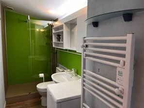 A modern bathroom with a green shower enclosure, a white toilet, a white sink, and a white towel rack.